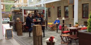 Two men sat facing each other drinking coffee at a small, round table outside Noco Kiosk inside Westgate Arcade, Halifax.